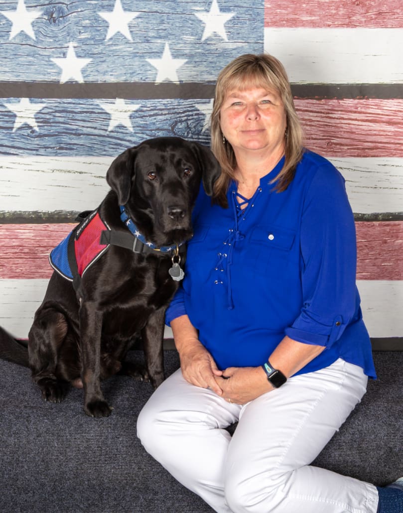 A woman sitting next to her dog in front of an american flag.