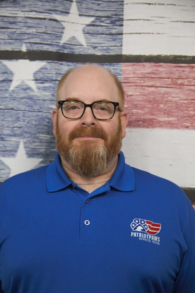 A man with a beard and glasses in front of an american flag.