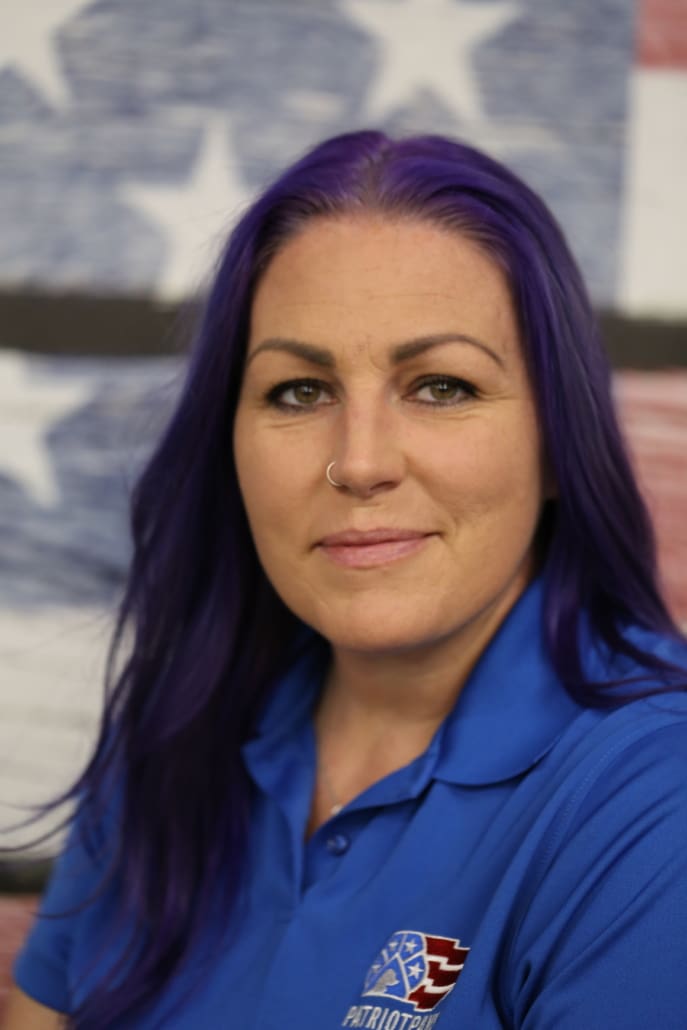 A woman with purple hair is smiling for the camera.