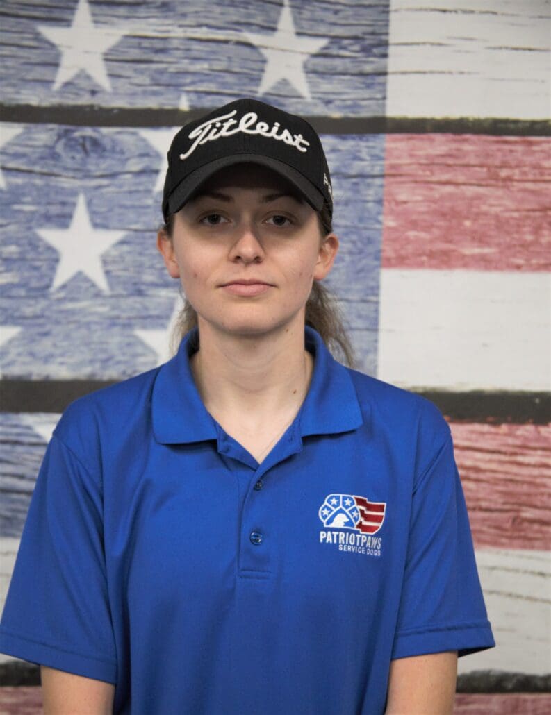 A woman in blue shirt and hat standing next to an american flag.