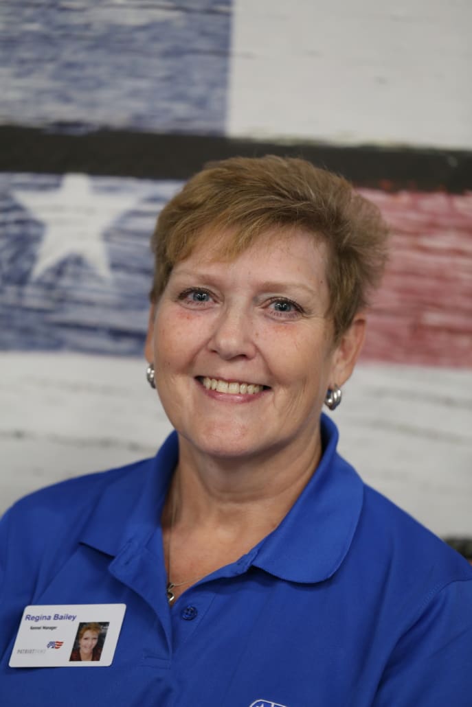 A woman in blue shirt standing next to an american flag.