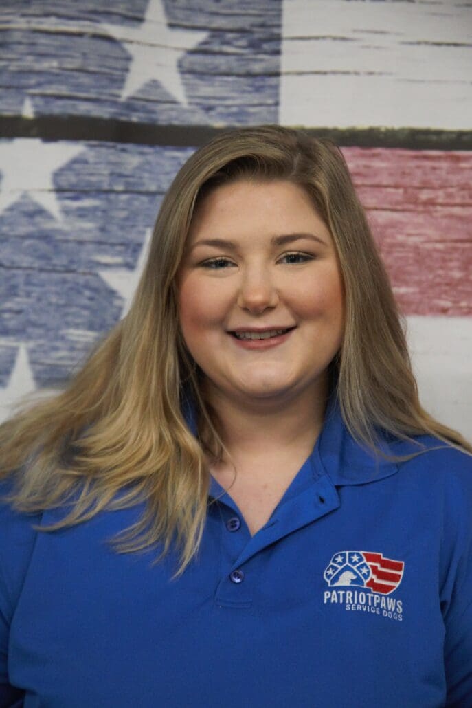 A woman in blue shirt standing next to an american flag.