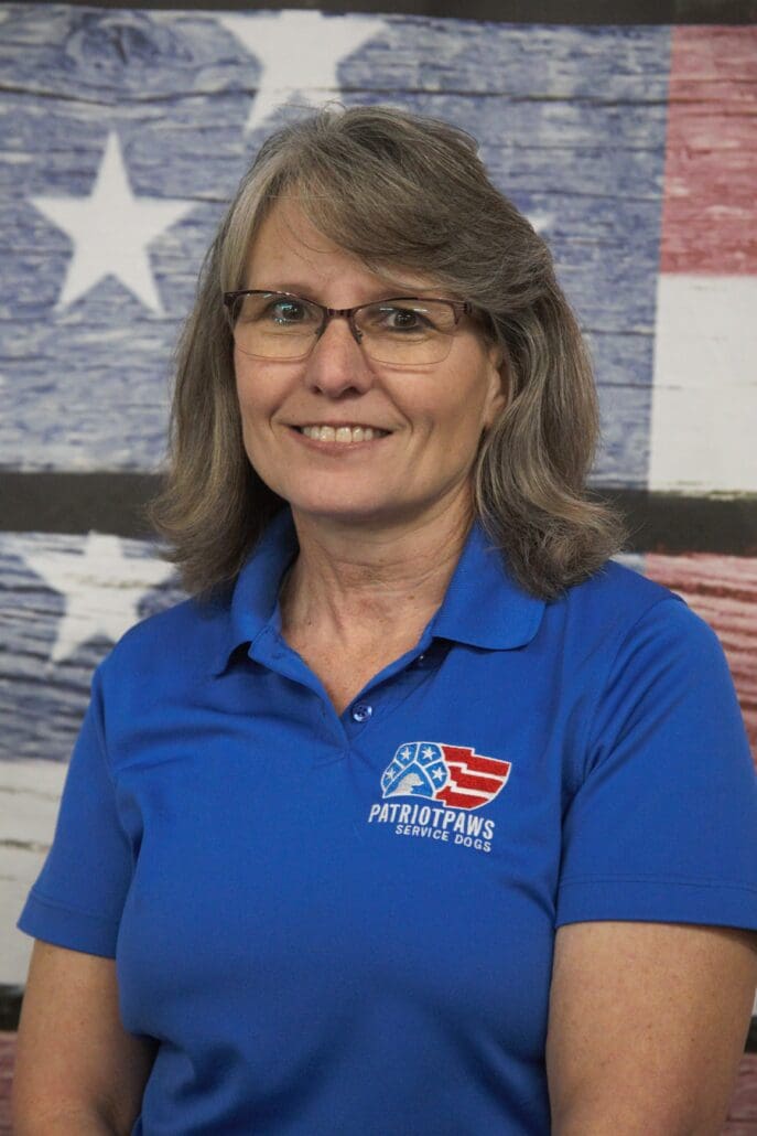 A woman in blue shirt standing next to american flag.