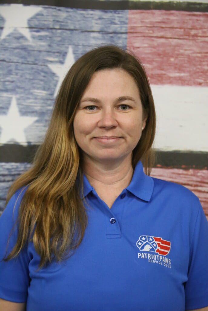 A woman in blue shirt standing next to an american flag.
