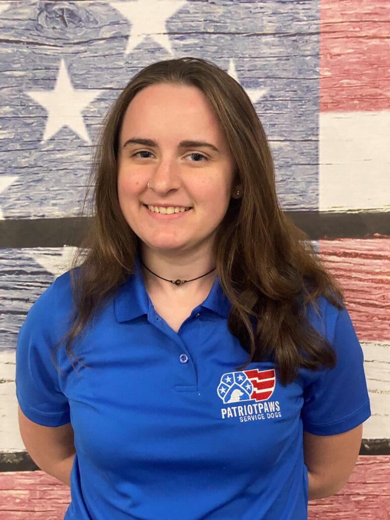 A woman in blue shirt standing next to an american flag.