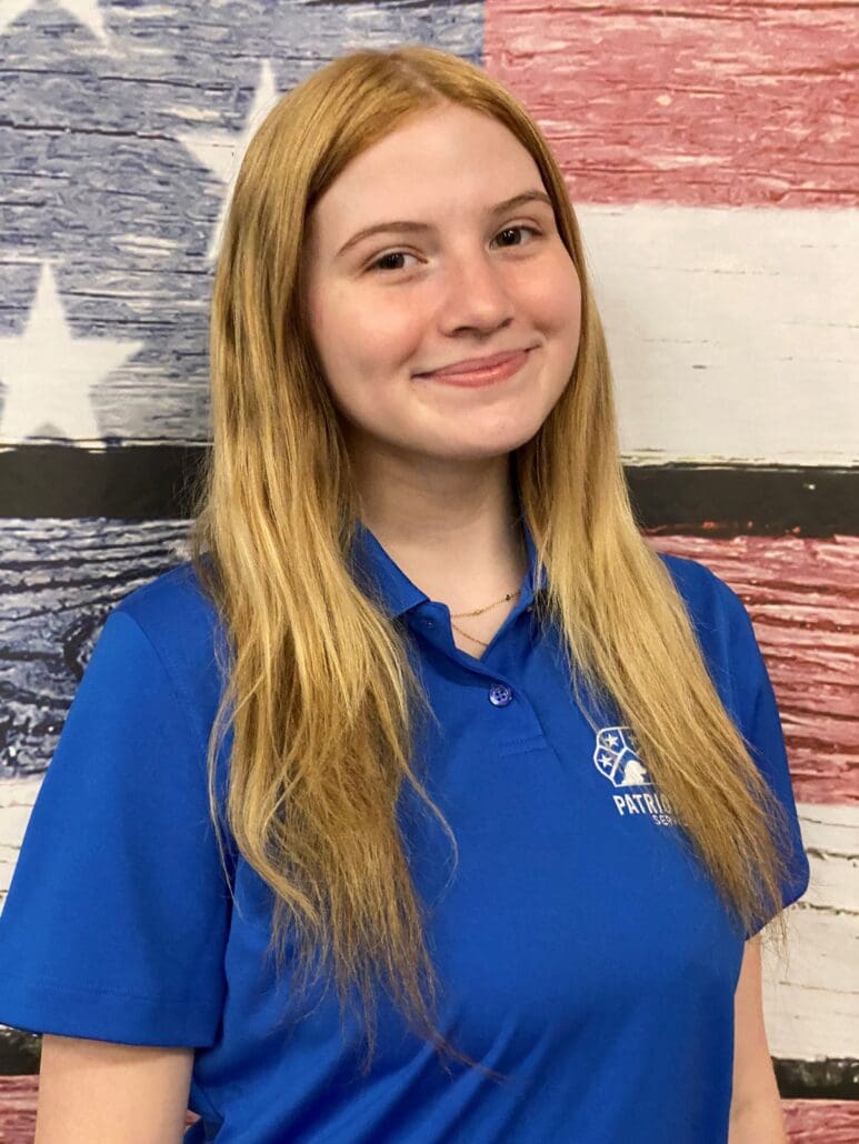 A girl in blue shirt standing next to american flag.